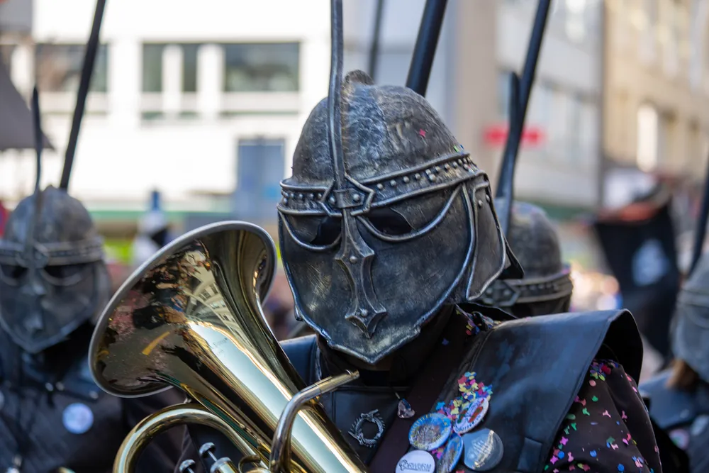 Guggenmusiker mit dunklem Ritterhelm als Grende spielt Euphonium, im Schallstück spiegelt sich die Strasse